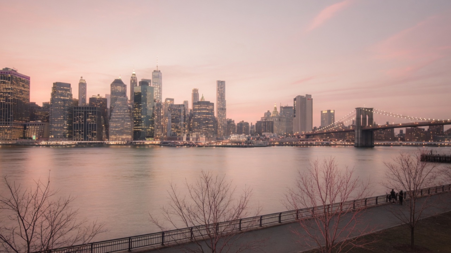 Waterfront view of the Manhattan skyline at dusk, with the Brooklyn Bridge on the right